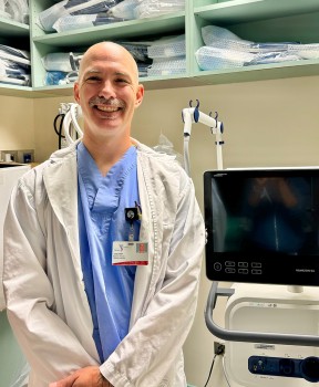 Craig Doell standing in a white coat and scrubs